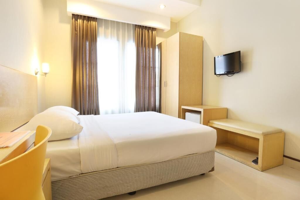 Ein Hotelzimmer mit Bett, Schreibtisch, Stuhl, Fernseher und einem fensterbepflanzten Fenster.
