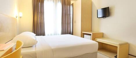 Ein Hotelzimmer mit Bett, Schreibtisch, Stuhl, Fernseher und einem fensterbepflanzten Fenster.