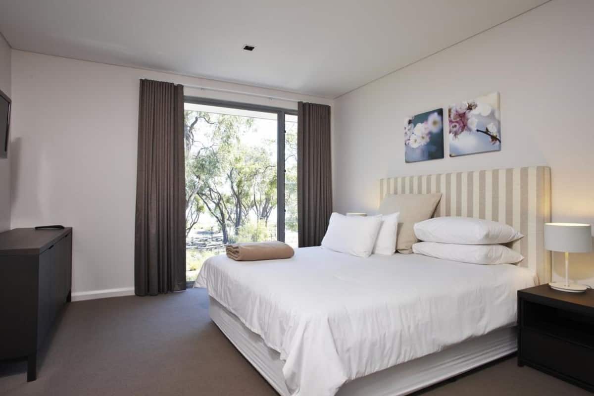 A modern hotel room with a large bed, a desk, and a window with curtains.