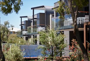 A modern building with multiple balconies and glass railings, surrounded by greenery and trees. - Aqua Resort Busselton (Broadwater)