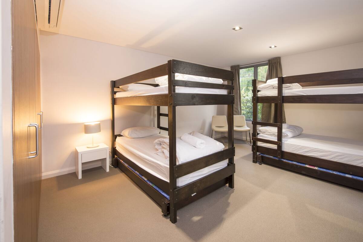 A room with two bunk beds, a bedside table with a lamp, and a window with curtains.