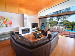 A modern living room with a fireplace, leather sofa, and a large glass door leading to an outdoor patio. - Aqua Resort Busselton (Broadwater)