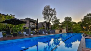 A swimming pool with lounge chairs and umbrellas, surrounded by greenery and a modern building. - Aqua Resort Busselton (Broadwater)