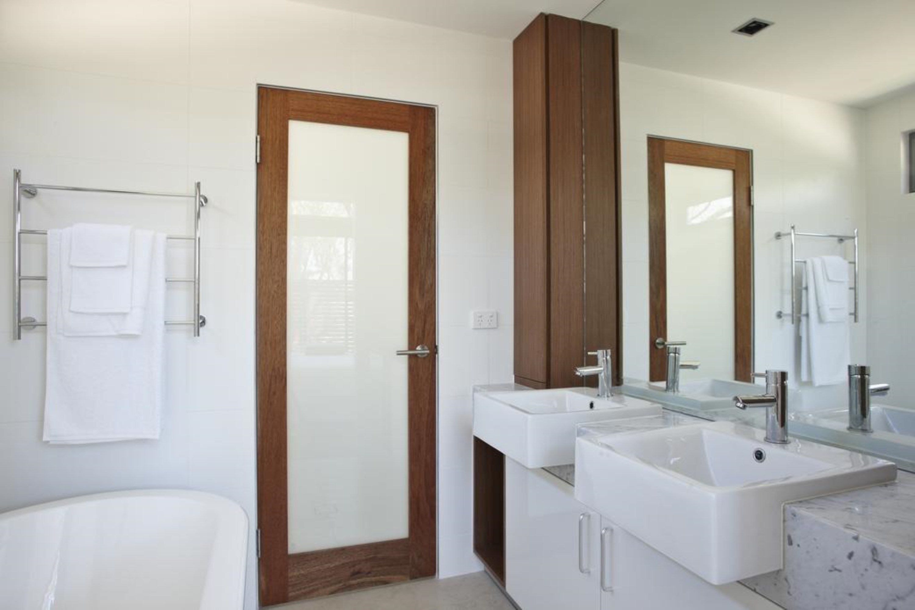 Un bagno moderno con una porta in legno, due lavabi, una vasca e uno specchio grande.