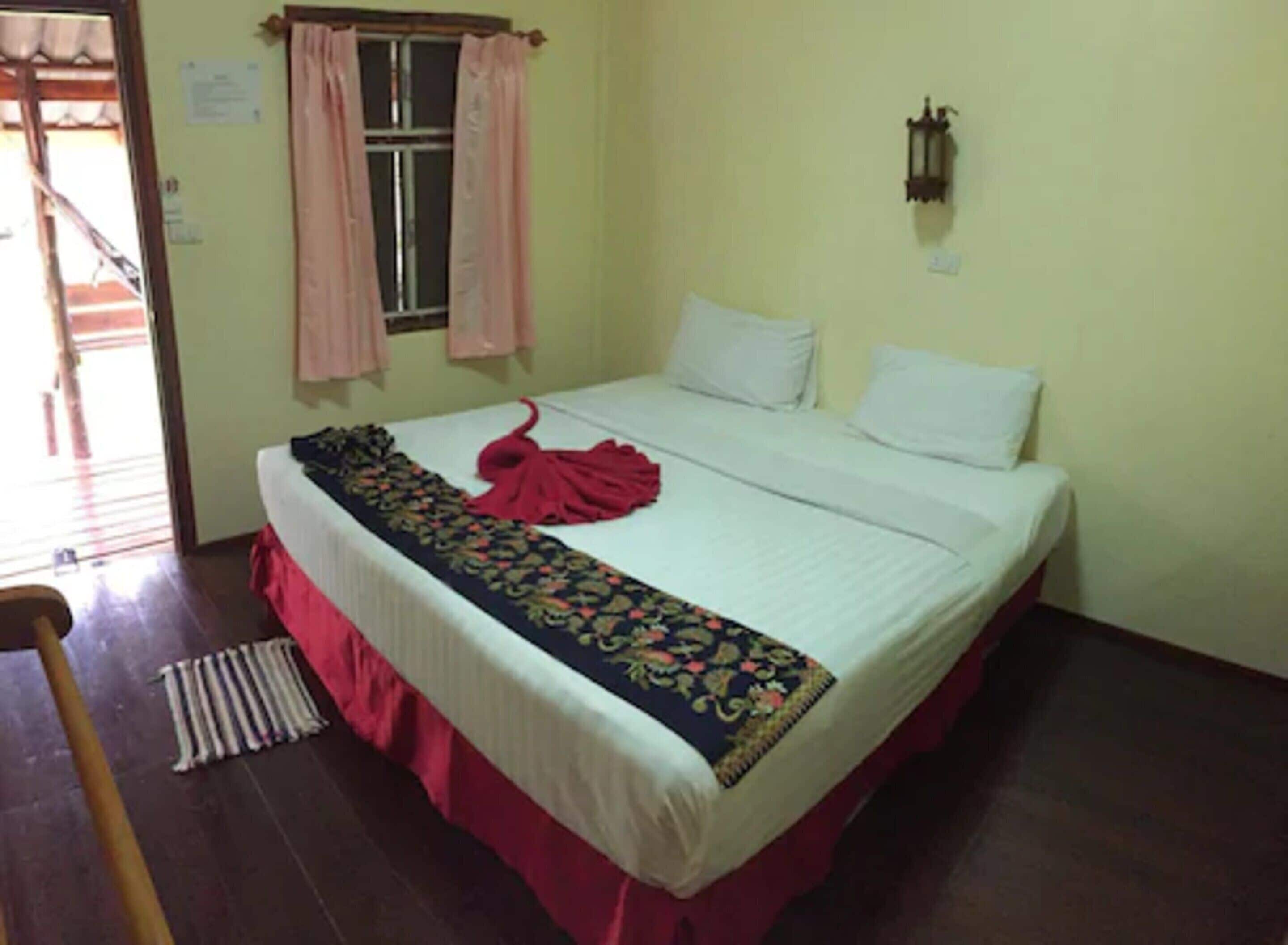 A room with a bed, a window with curtains, a wall-mounted light fixture, and a door.