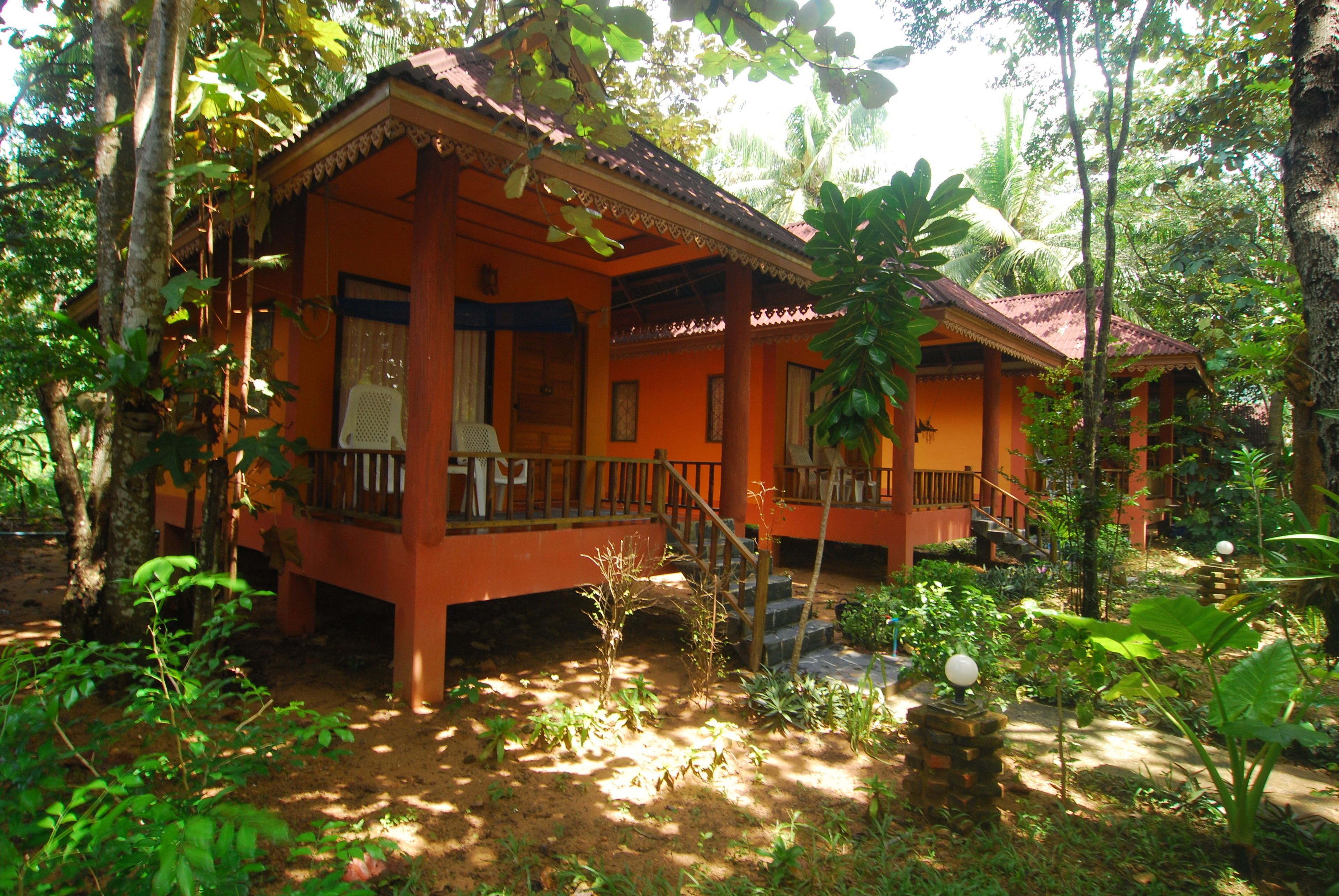 A traditional wooden house with a porch, surrounded by lush greenery.