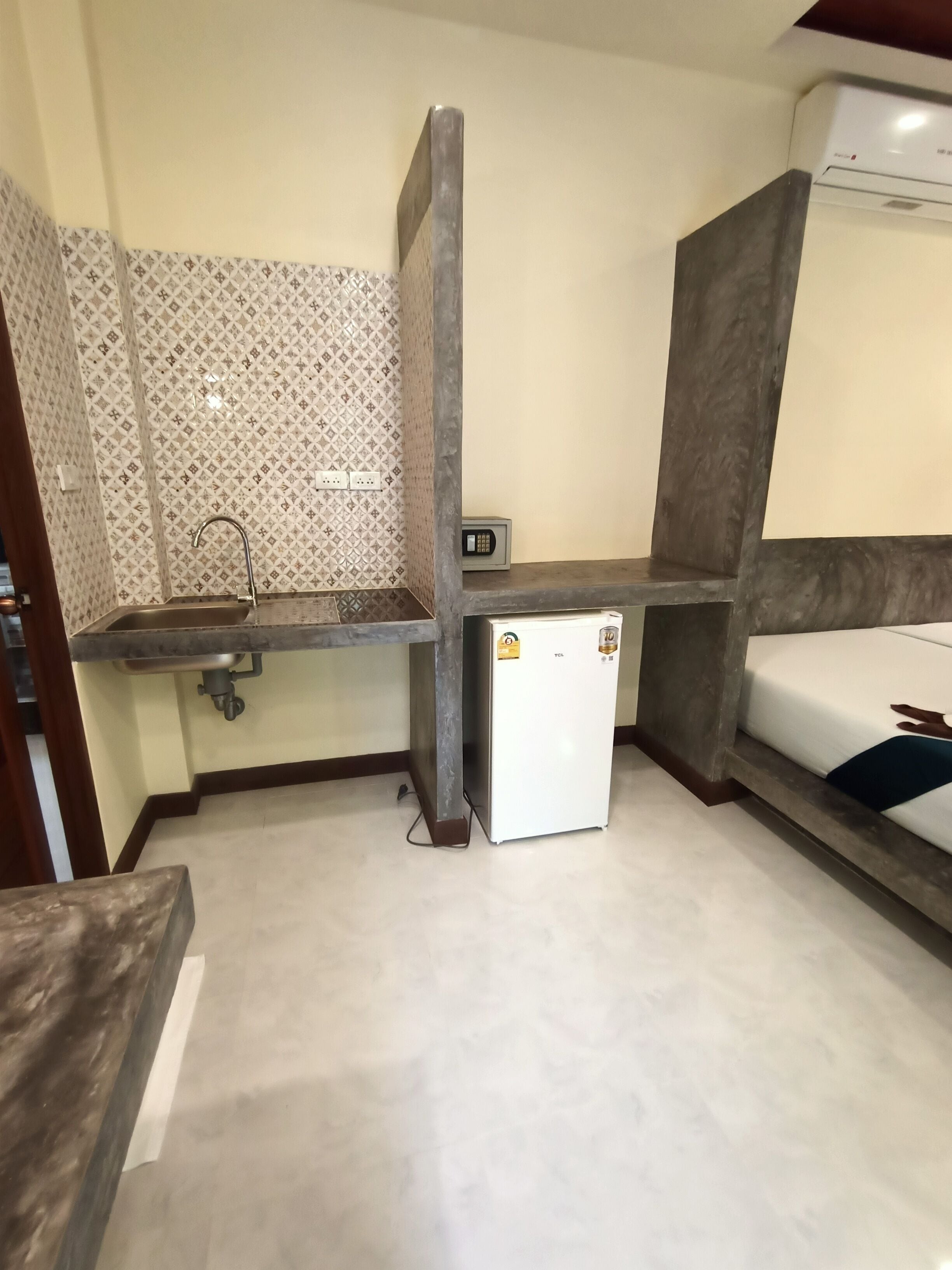 A compact hotel room with a kitchenette, a small fridge, a bed, and a wall-mounted air conditioner.