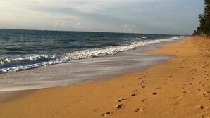 Praia arenosa com pegadas que levam à água, céu claro e mar calmo.