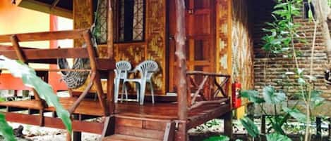 Una casa de madera con un porche, dos sillas de plástico blanco y una pequeña escalera que lleva a la entrada.