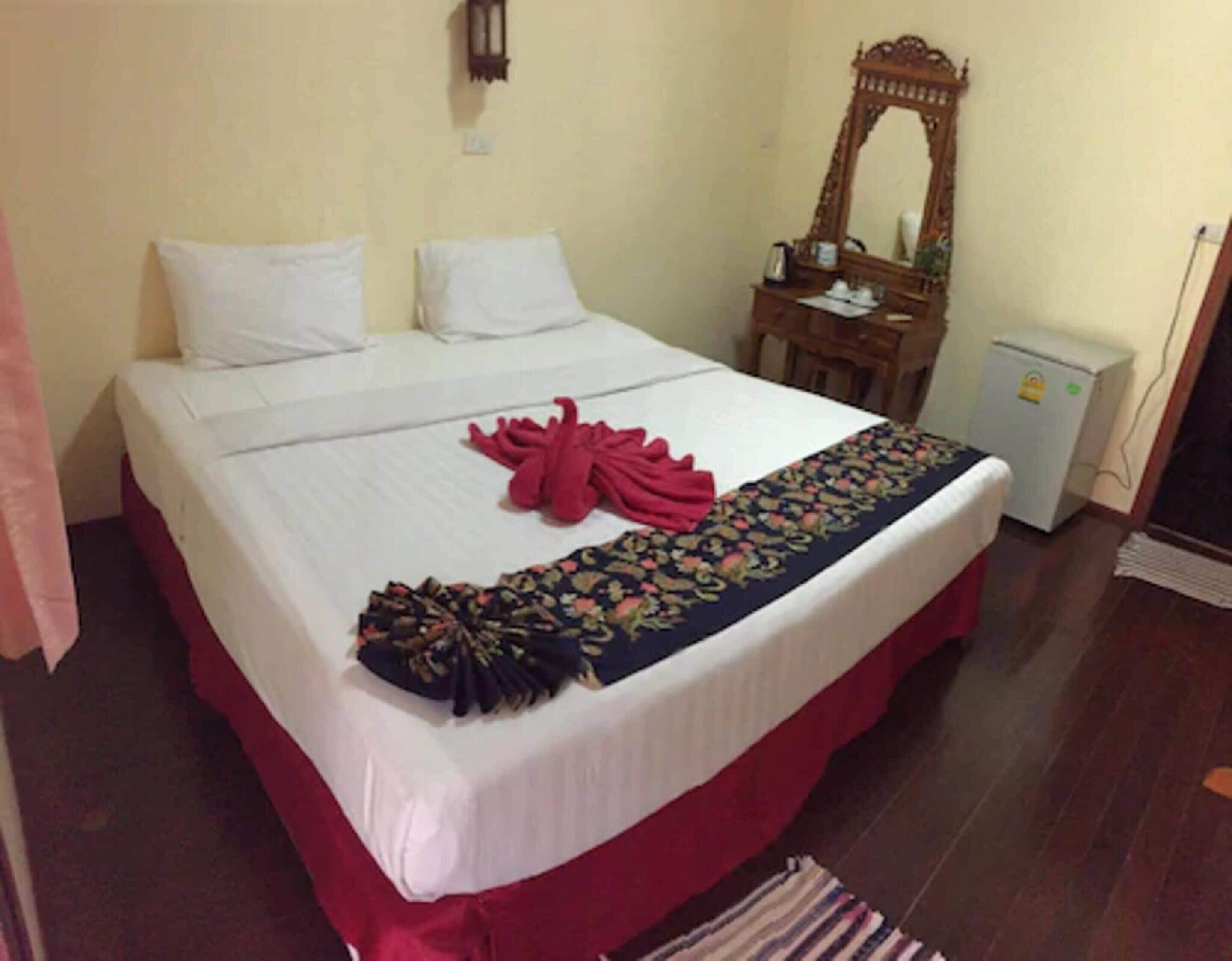 Cama bem arrumada com lençóis brancos, um corredor estampado com flores e toalhas vermelhas.
