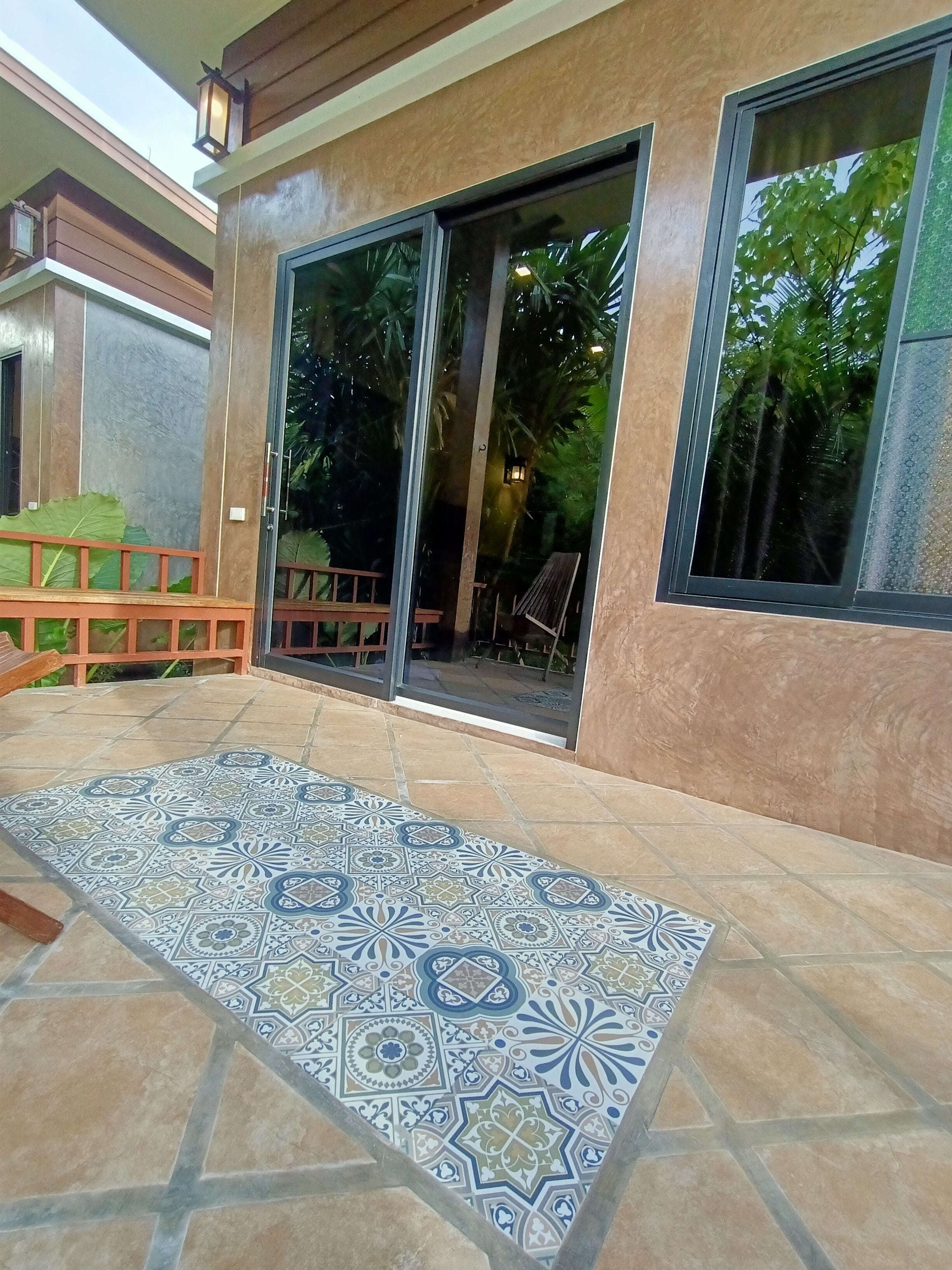 Un patio con baldosas estampadas, un banco de madera y una puerta corrediza de vidrio que da a un espacio exterior cubierto.