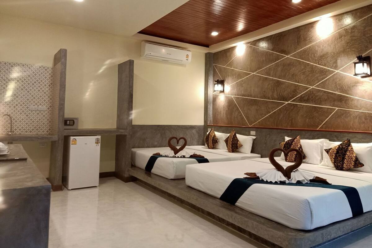 Une chambre d’hôtel avec deux lits, une petite kitchenette, un appareil de climatisation et un mur décoratif orné de motifs géométriques.