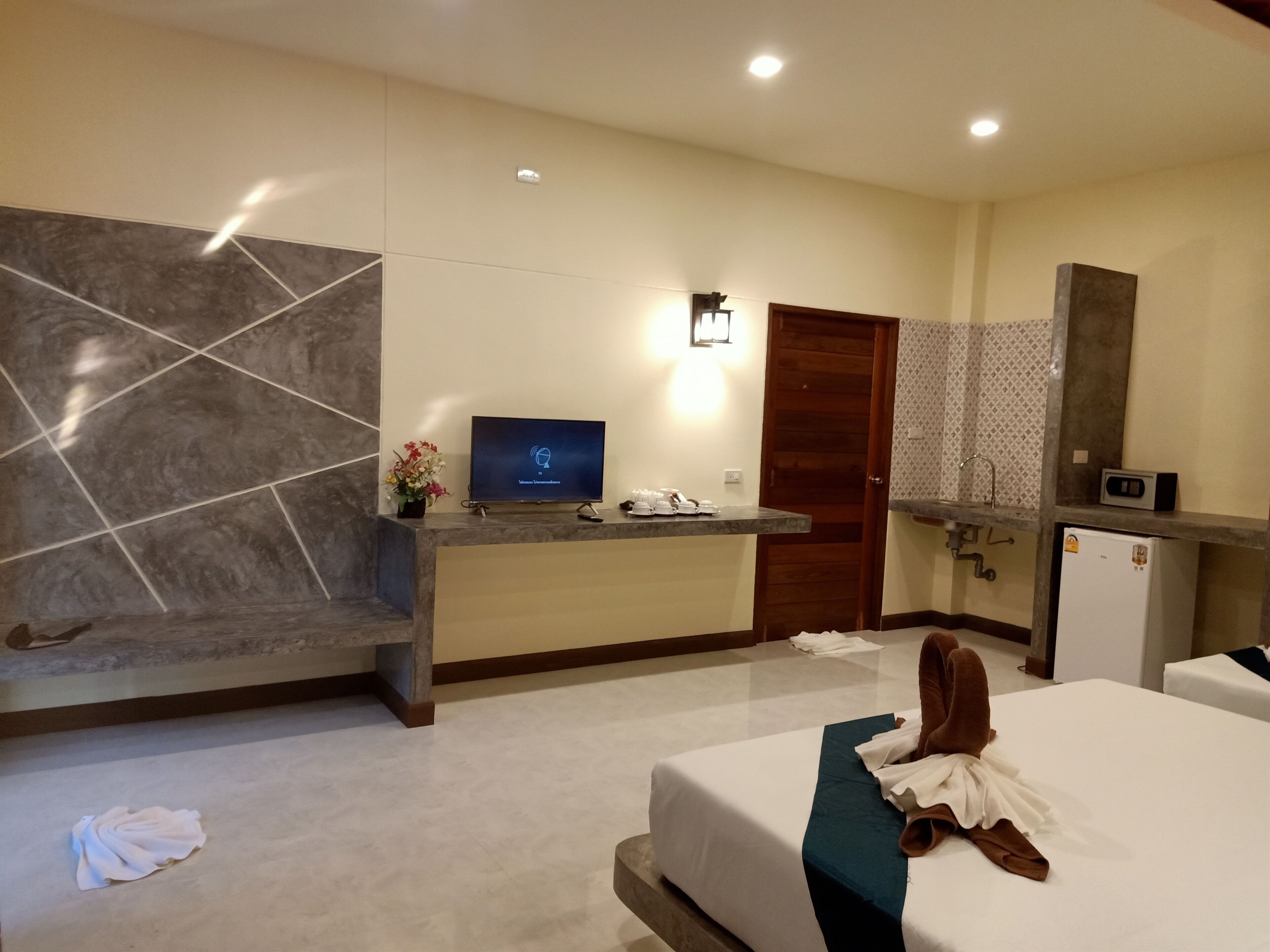 Habitación de hotel con cama, escritorio con televisor de pantalla plana, refrigerador pequeño, espejo y baño con cortina de ducha estampada.
