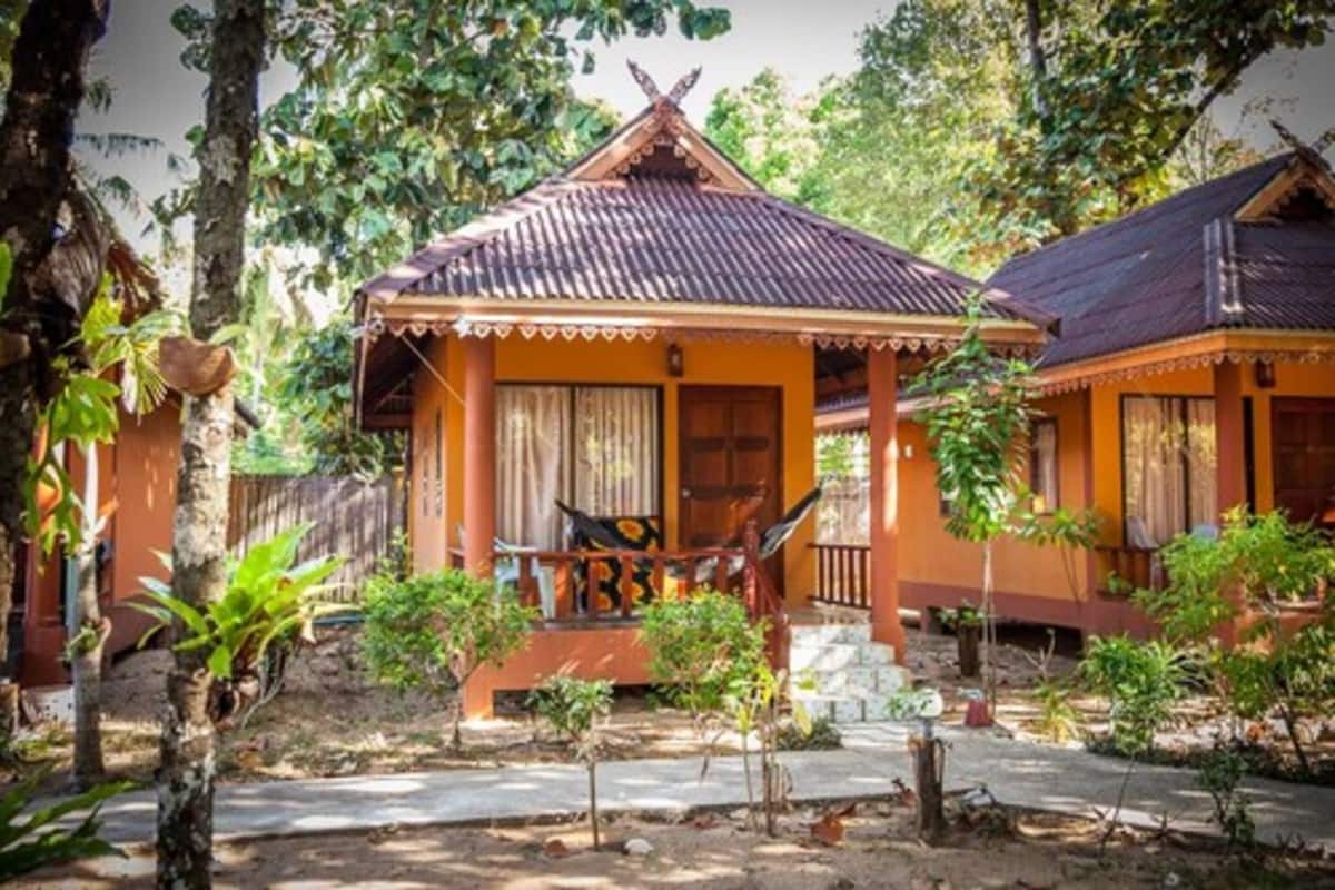 Une maison traditionnelle avec un toit en tuiles, une véranda avec un hamac et un petit jardin.