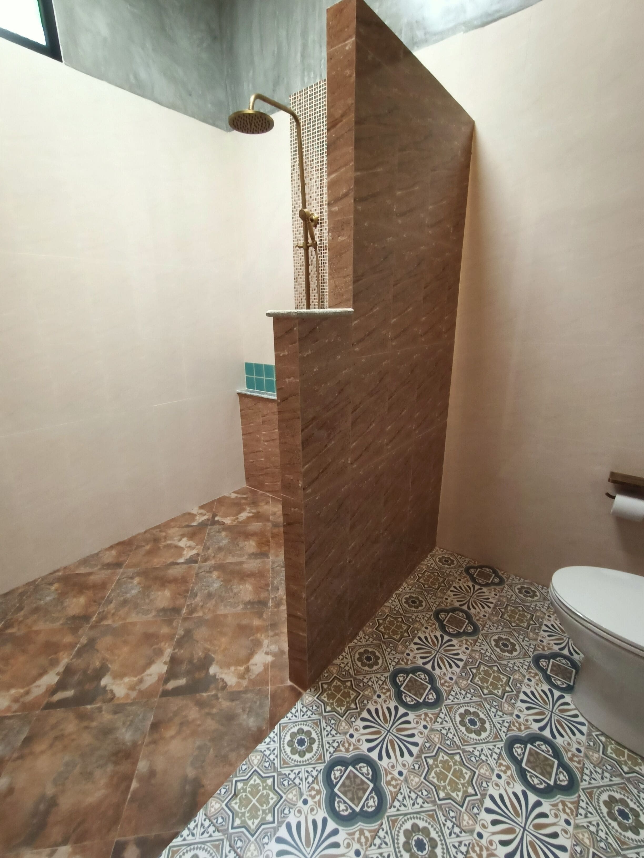 A bathroom with a shower, a toilet, and patterned floor tiles.