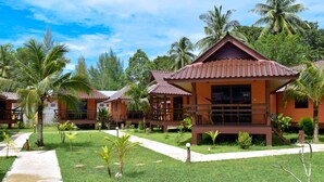 Resort com várias construções no estilo de bangalô, cada uma com telhado de cerâmica e cercada por vegetação exuberante e palmeiras.