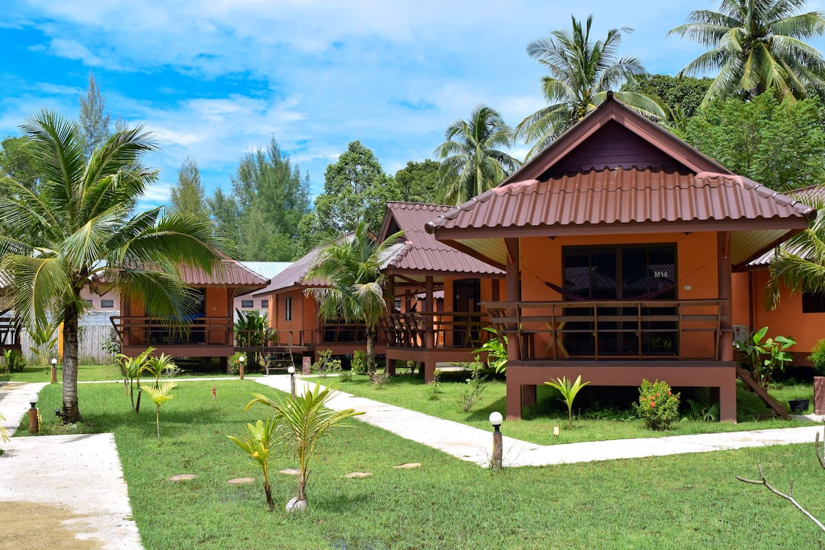 Un complexe hôtelier comprenant plusieurs bâtiments de style bungalow, chacun doté d’un toit en tuiles et entouré d’une végétation luxuriante et de palmiers.