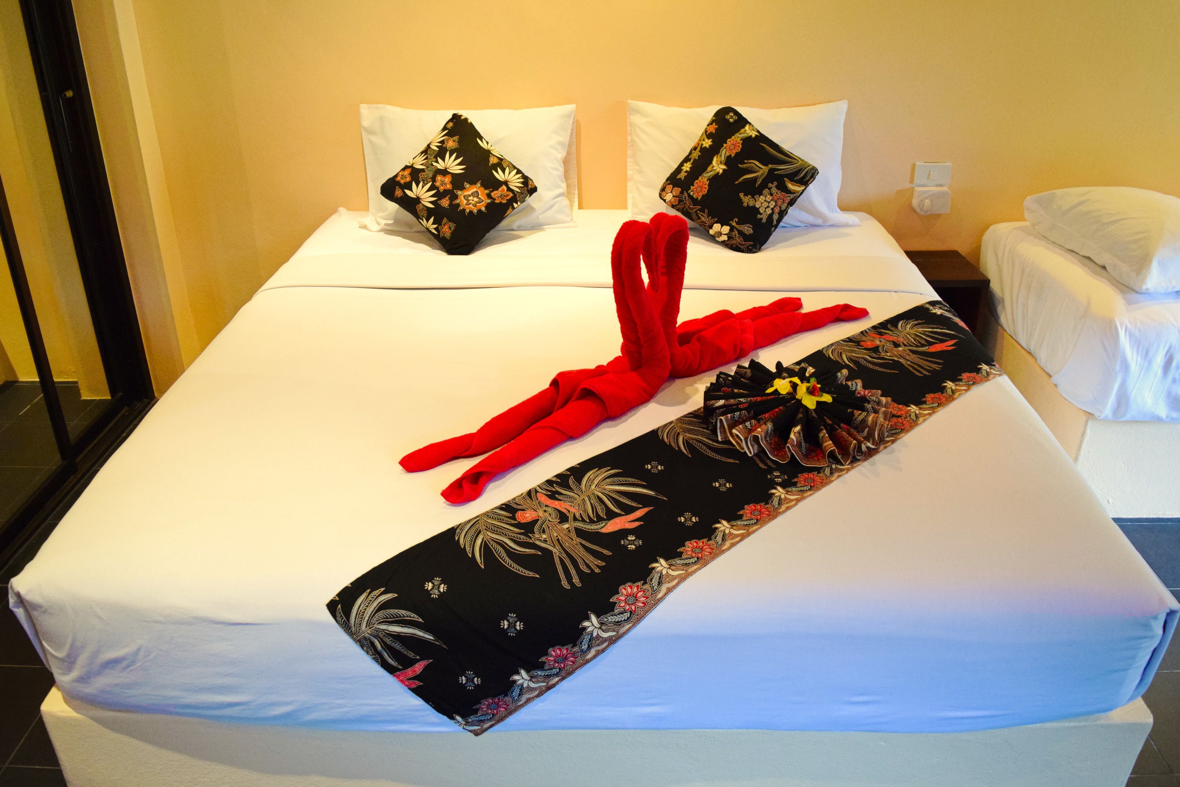 A hotel room with a neatly made bed, floral-patterned bedspread, and a red towel.