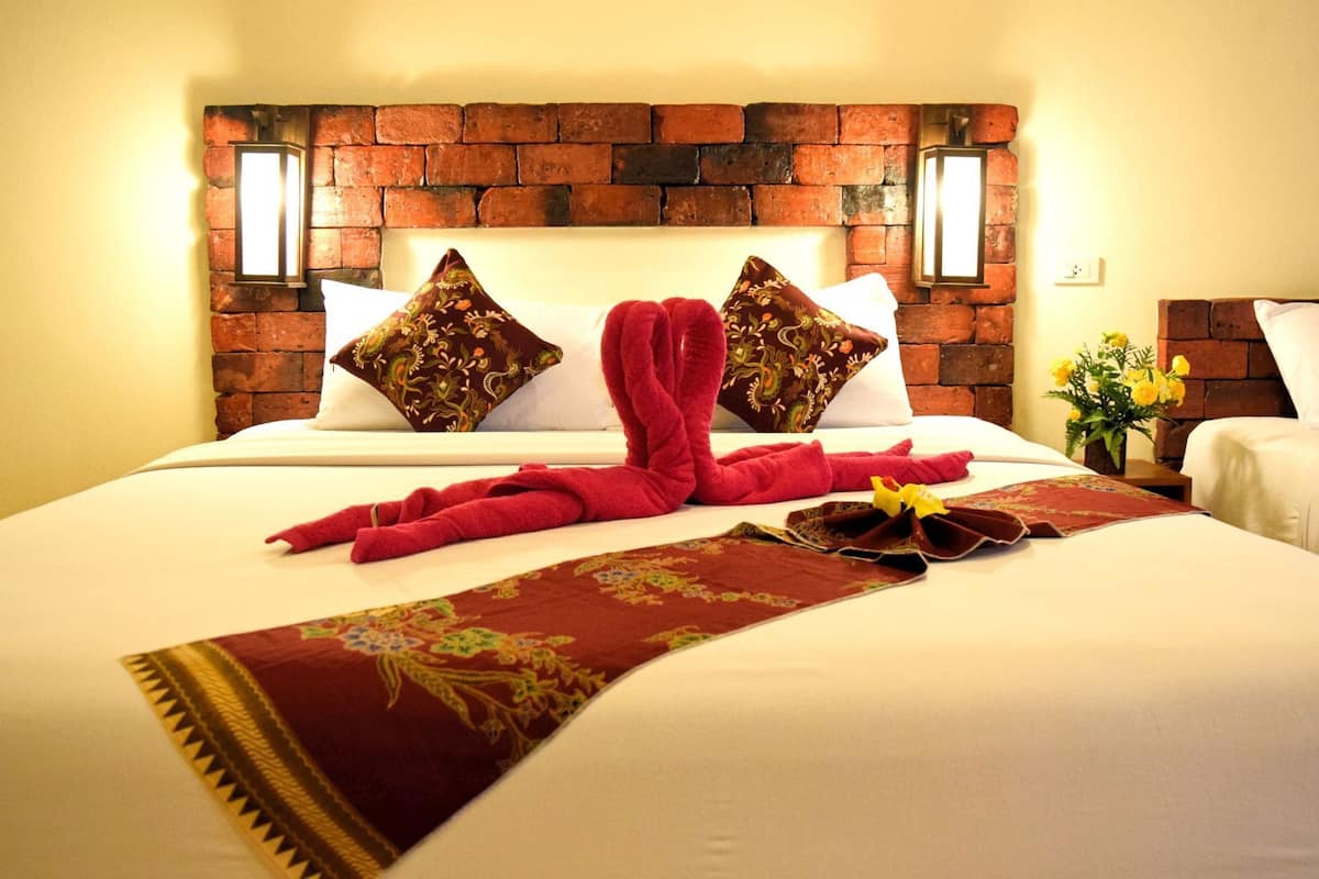 Une chambre d’hôtel avec une tête de lit en briques, deux coussins décoratifs, une serviette rouge et une couvre-lit à motifs floraux.