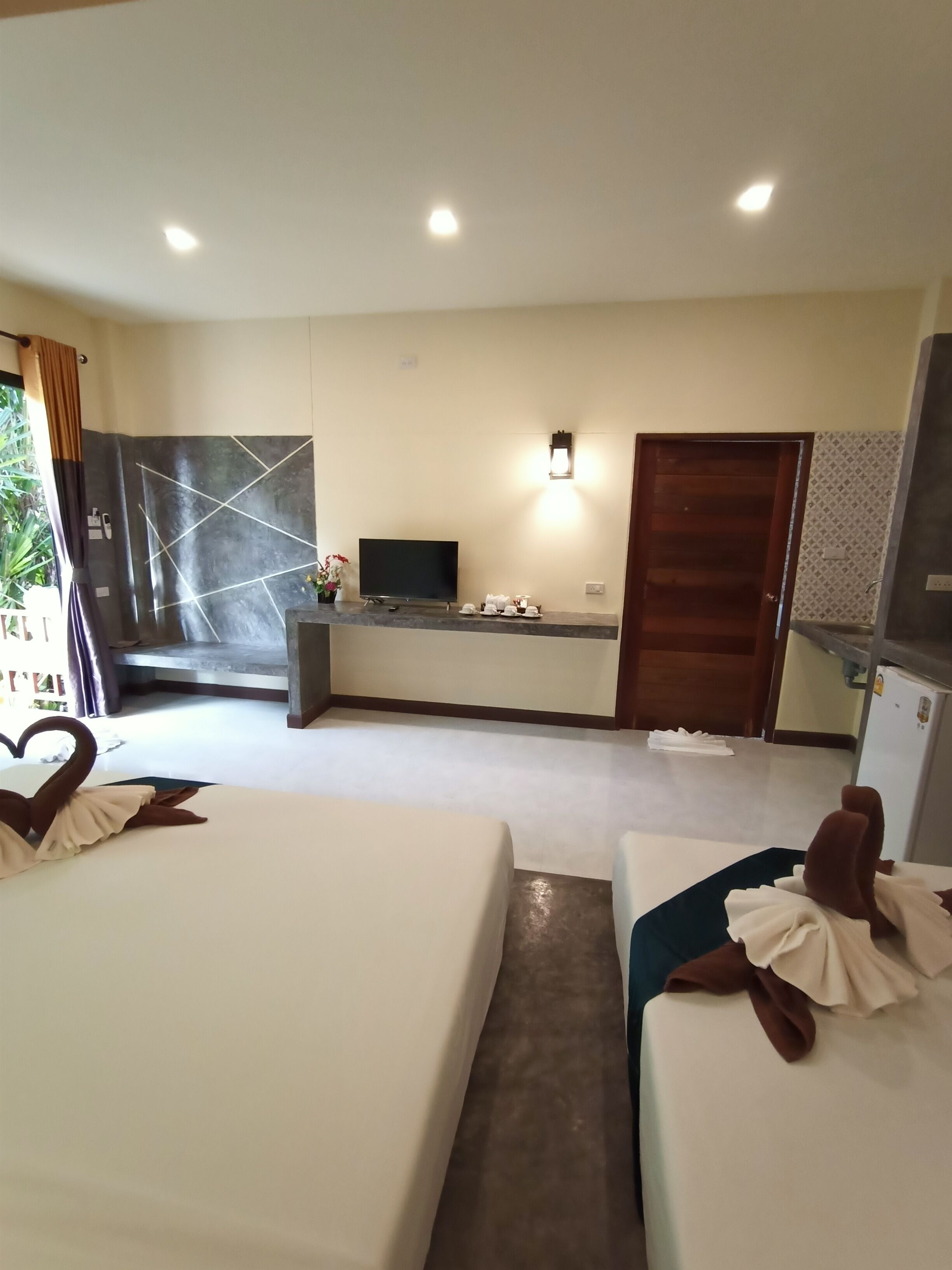 A hotel room with two beds, a desk with a flat-screen TV, a wall-mounted light, and a door.