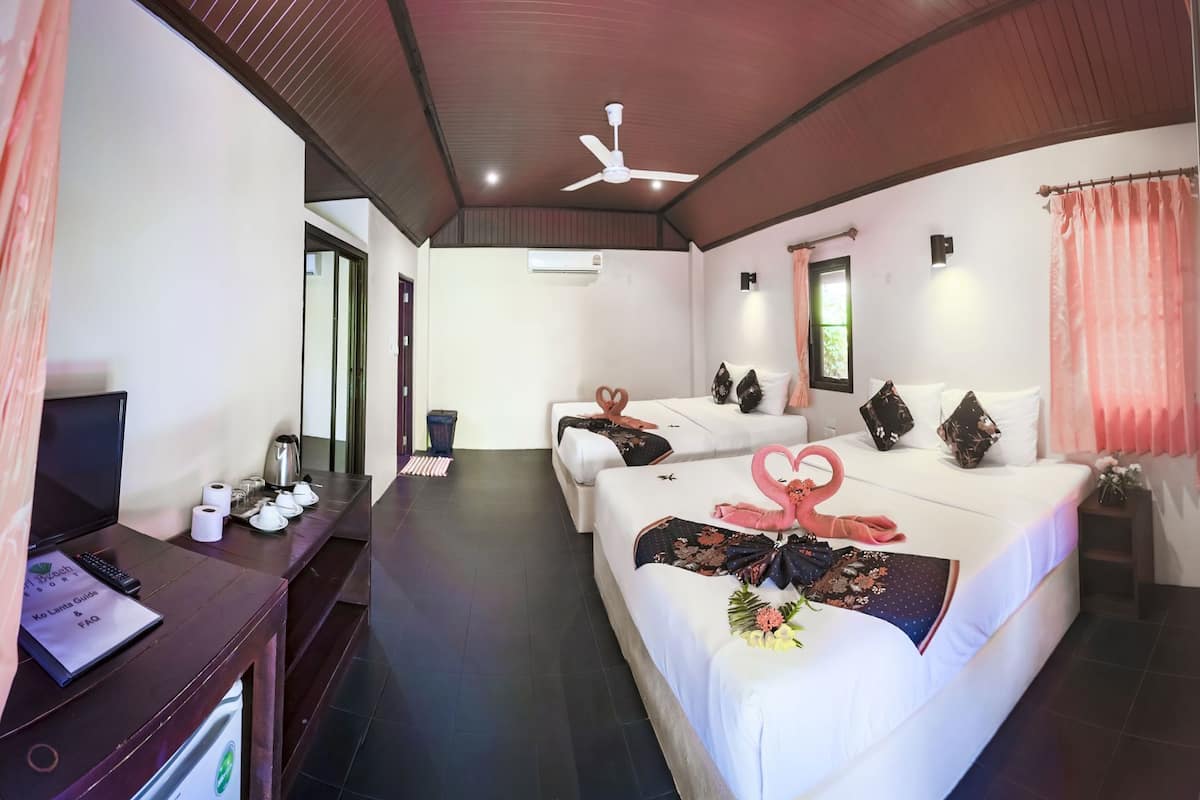 Une chambre d’hôtel avec deux lits, un ventilateur de plafond, une télévision et un bureau équipé d’un ordinateur portable et d’une télécommande.
