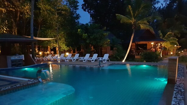 Piscina com água azul cristalina, cercada por espreguiçadeiras brancas e uma palmeira.