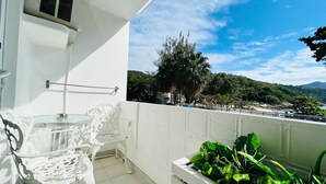 A balcony with a white chair, a small table, and a planter with green plants.
