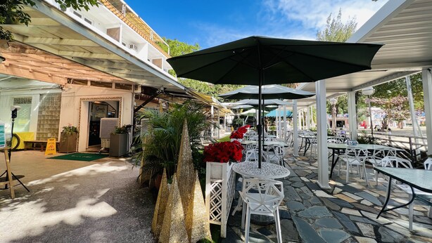 An outdoor patio area with white tables and chairs, umbrellas, and potted plants.
