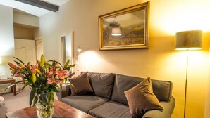 A living room with a brown leather sofa, a wooden coffee table with a vase of flowers, a painting on the wall, and a floor lamp. - Six Brunton Place (Edinburgh)