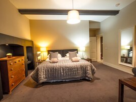 A bedroom with a large bed, wooden dresser, bedside lamps, and a hanging light fixture.