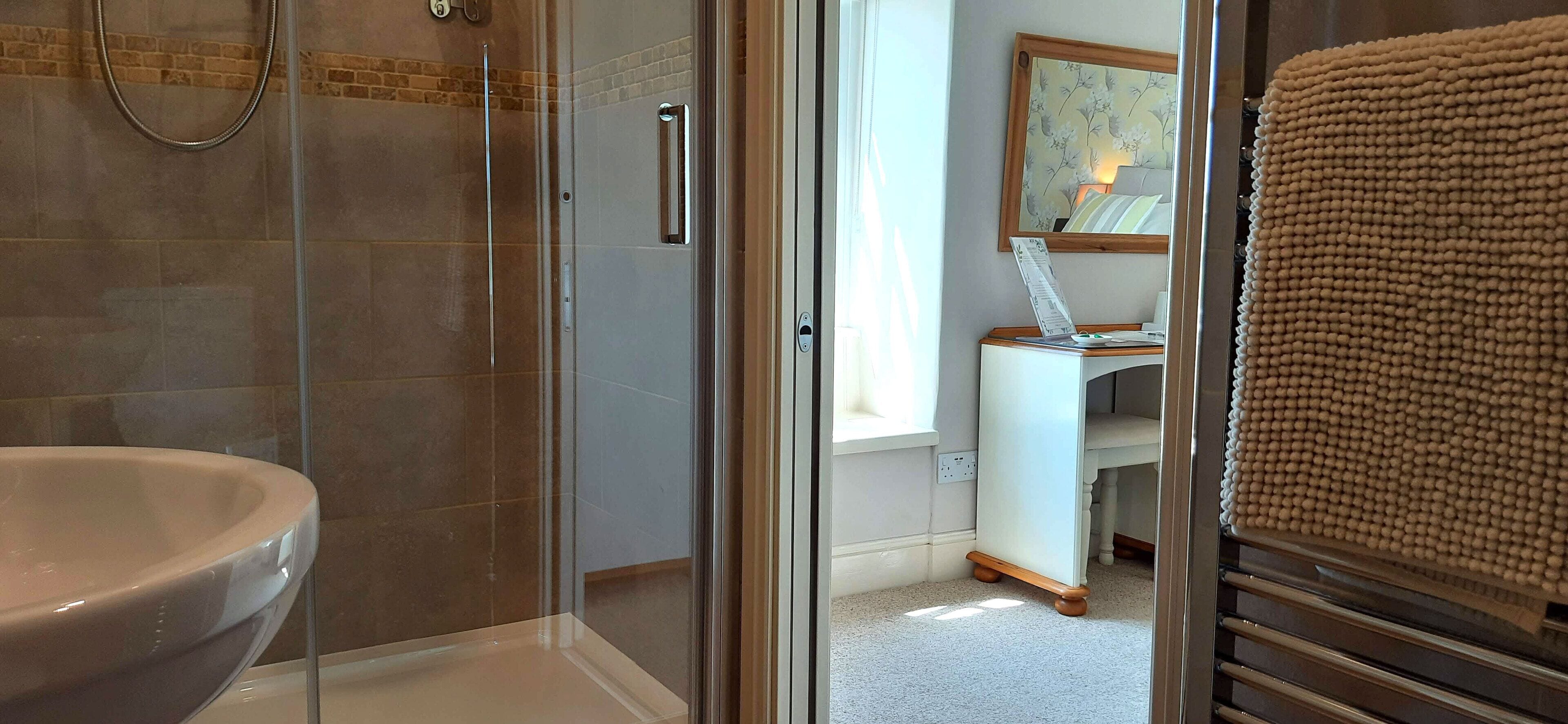 A bathroom with a glass-enclosed shower, a white sink, and a wooden towel rack.