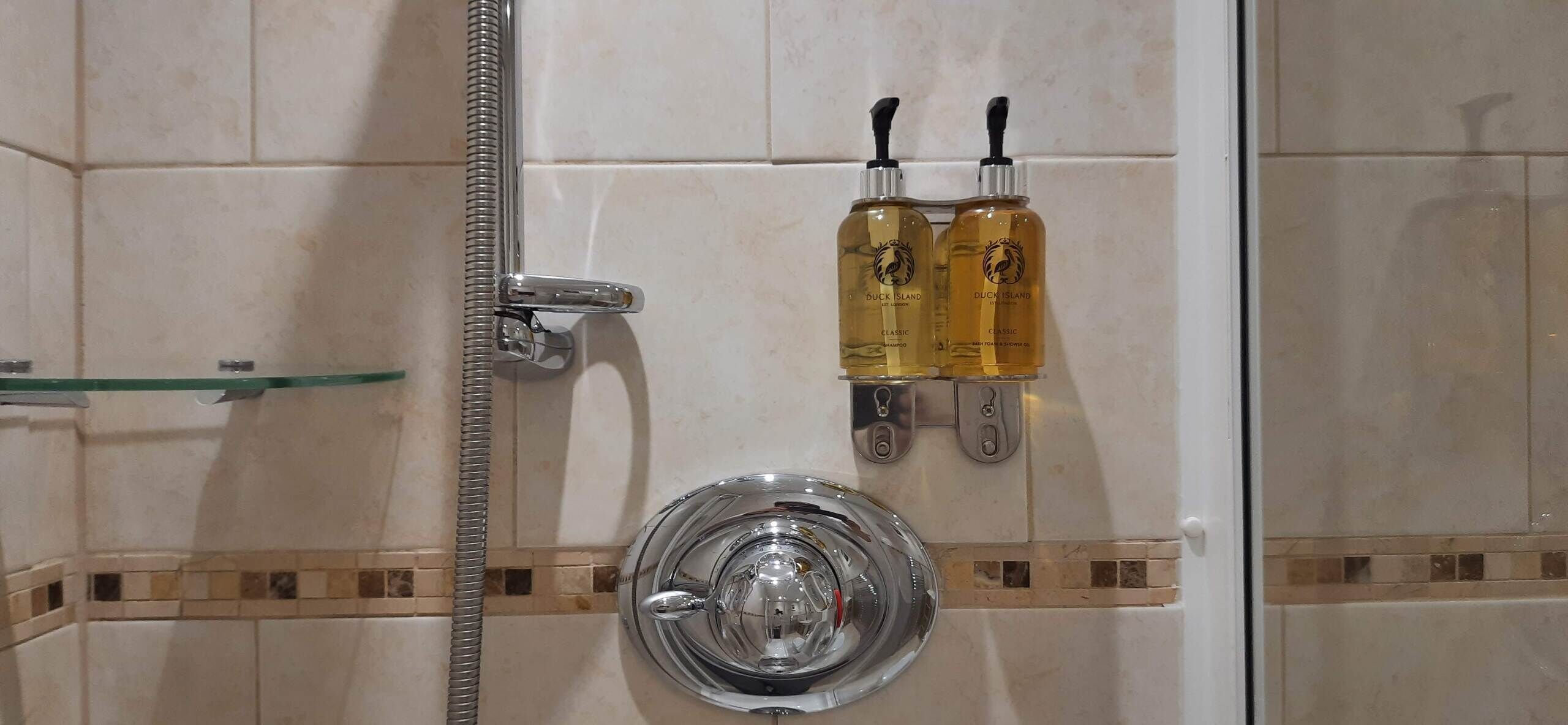 Un bagno con doccia, due flaconi di shampoo Duck Island Classic e un soffione cromato.