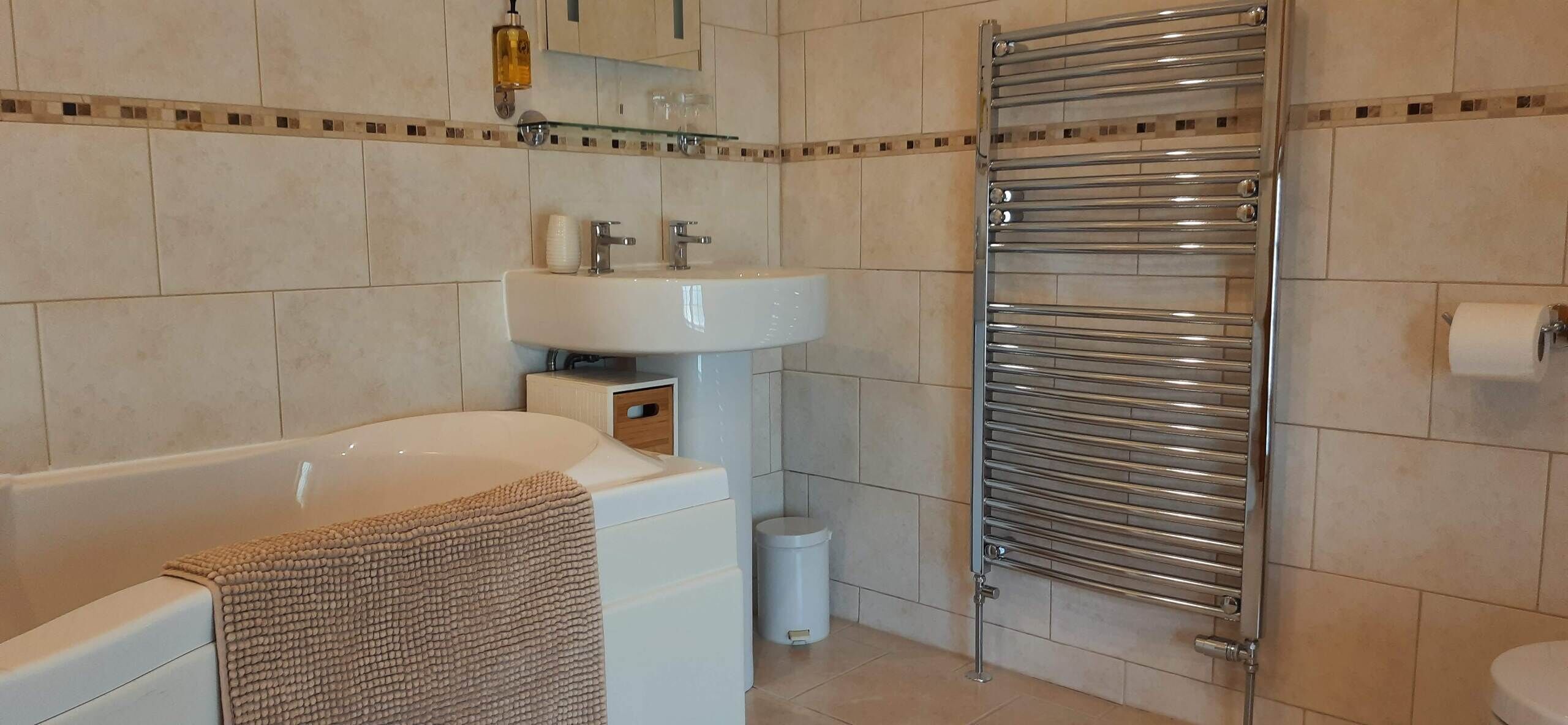 A modern bathroom with a bathtub, a sink, a glass shelf, and a towel rack.