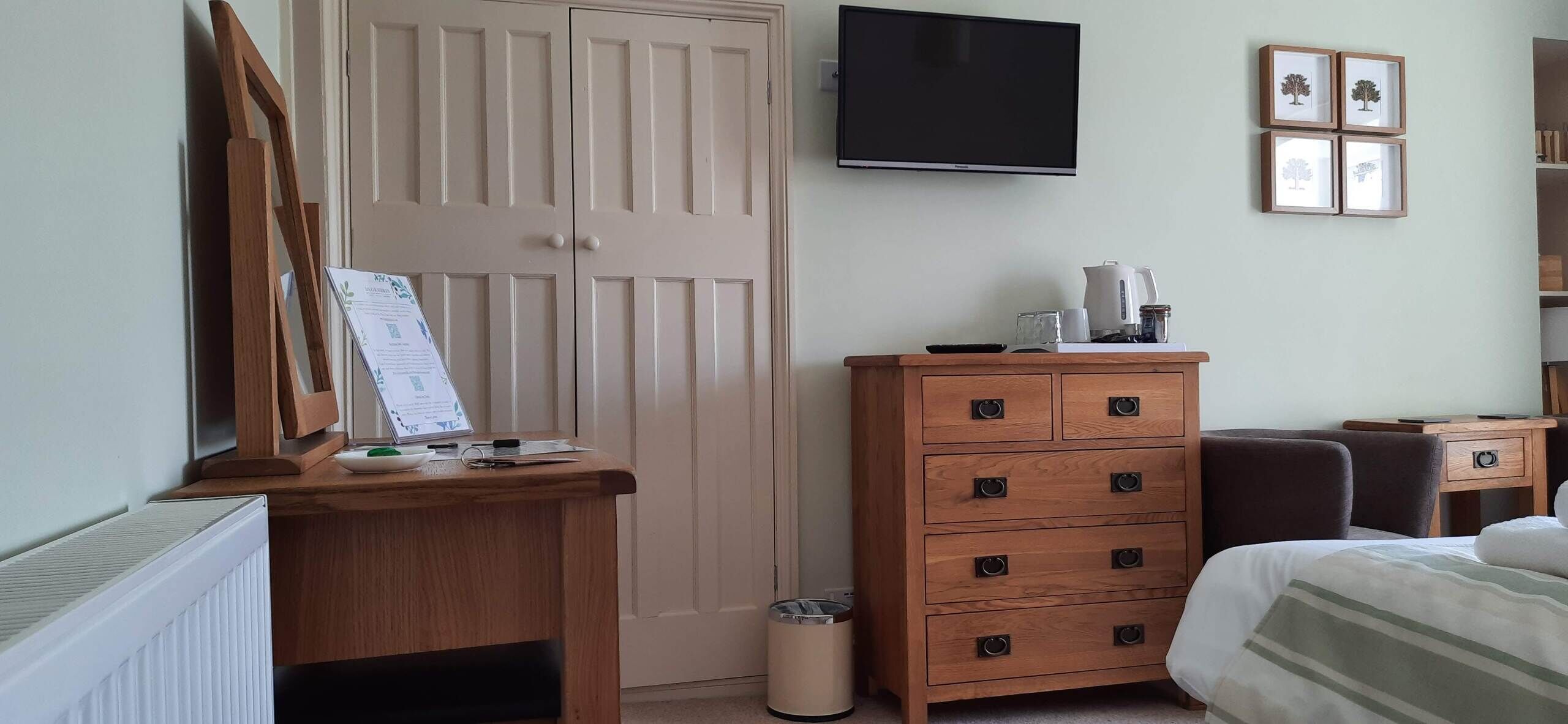 A bedroom with a wooden dresser, a bed, a TV, and a radiator.