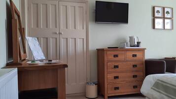 A bedroom with a wooden dresser, a bed, a TV, and a radiator.