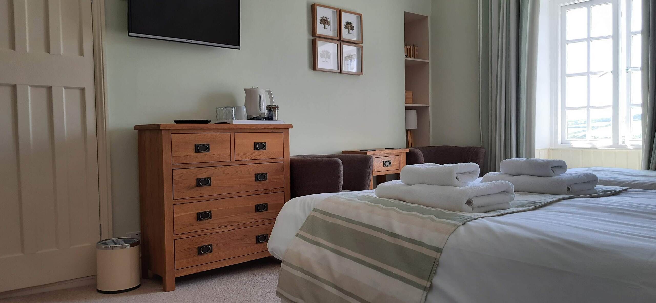 Een hotelkamer met een bed, een houten dressoir, een televisie en een raam met gordijnen.