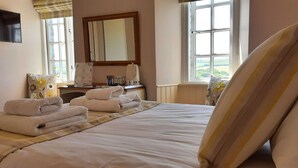 Quarto de hotel com cama, escrivaninha com computador, televisão de tela plana e janela com vista para o campo.