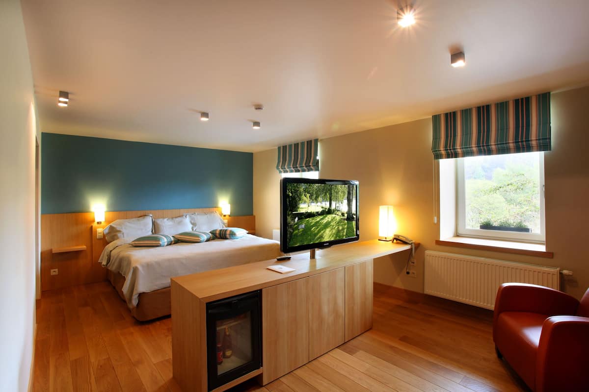 Een moderne hotelkamer met een bed, een televisie, een rode stoel en een raam met uitzicht op groen.