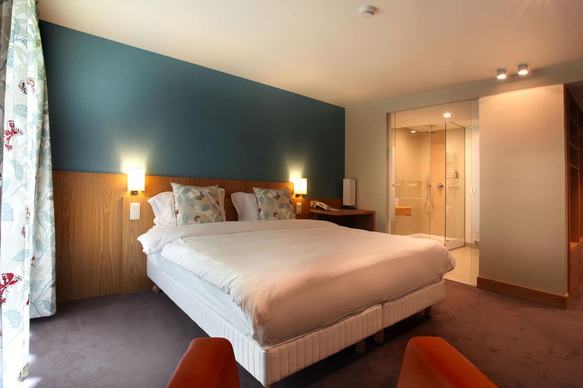 Een hotelkamer met een groot bed, nachtkastjes, een spiegel en een douche.