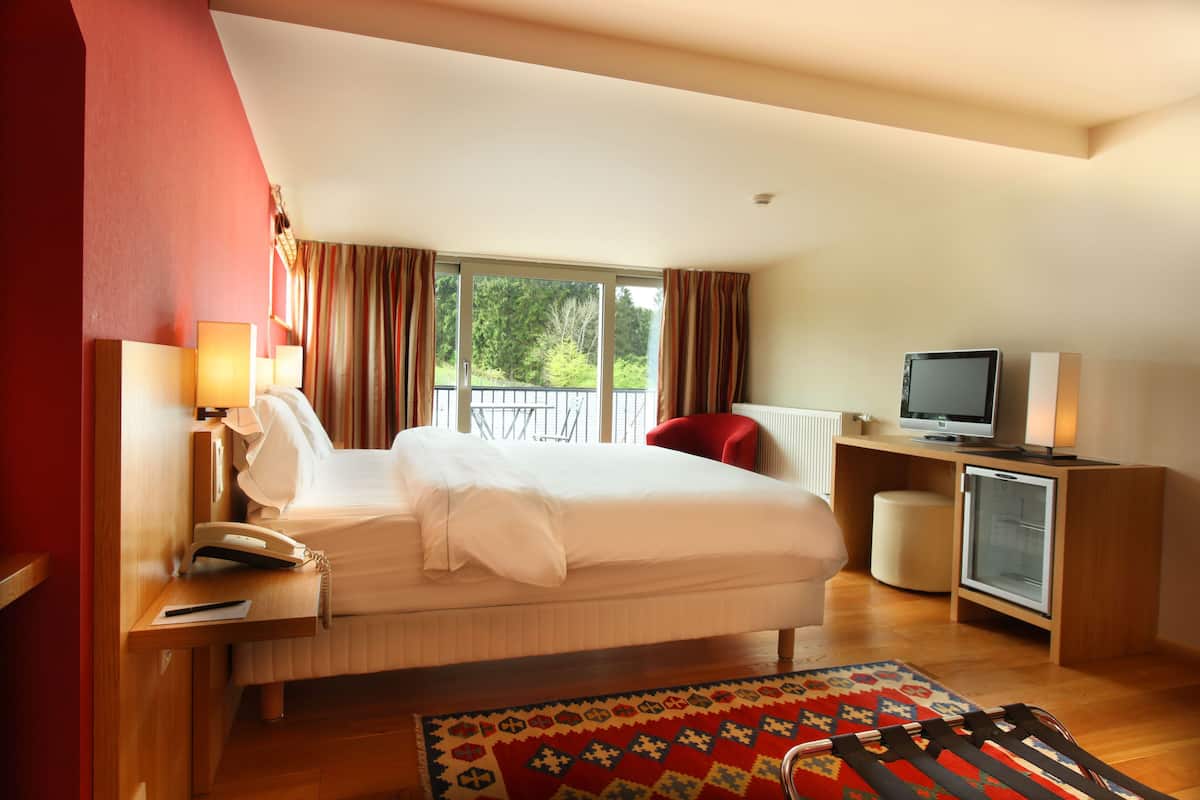 Hotelkamer met een bed, nachtlampjes, een televisie, een kleine koelkast en een raam met gordijnen.
