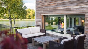 Een terras met een bank en stoelen, met uitzicht op een waterpartij en een gebouw met grote ramen.