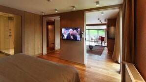 Een moderne hotelkamer met een groot bed, een aan de muur bevestigde televisie en uitzicht op het omliggende landschap door een schuifdeur.