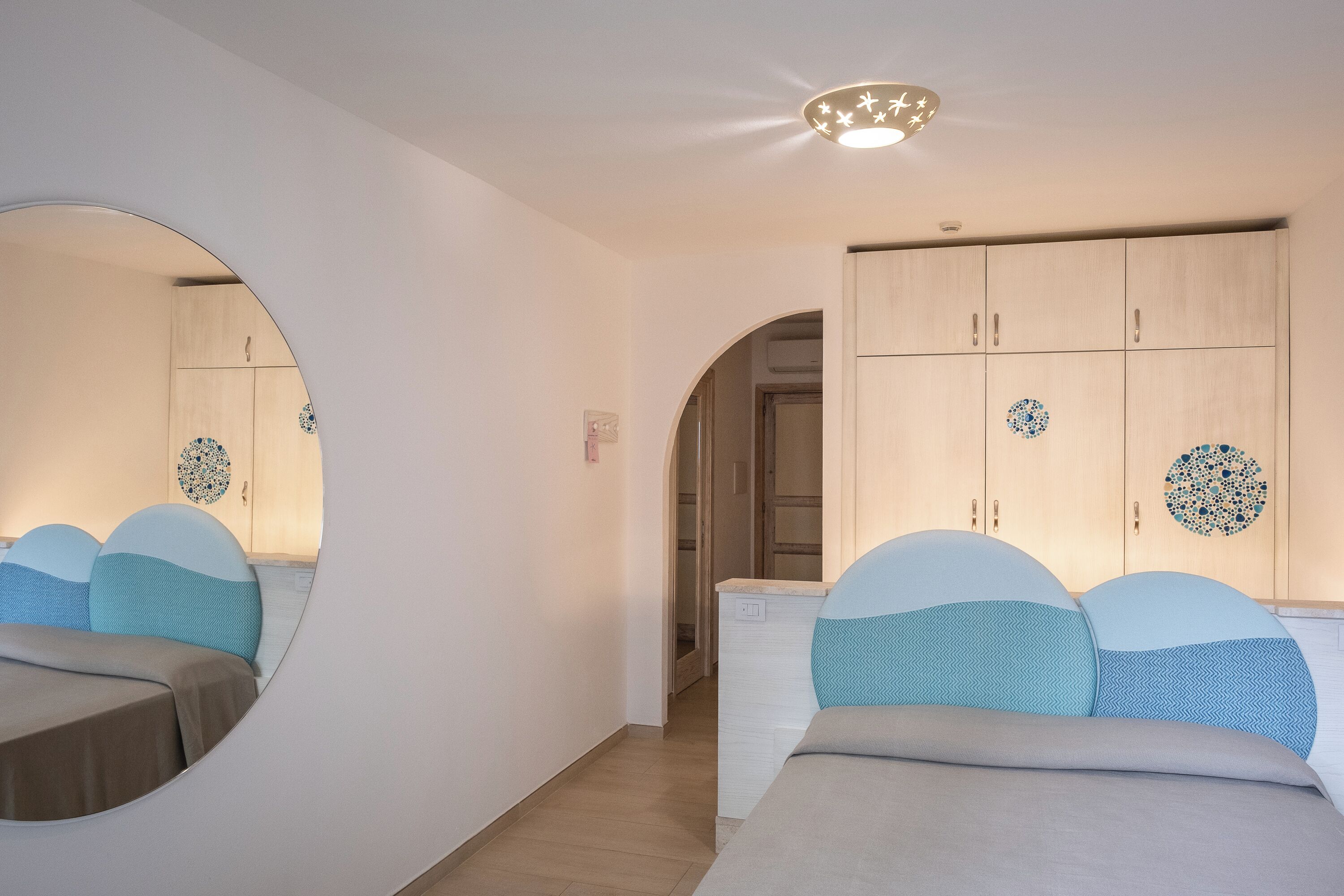 Ein Schlafzimmer mit einer Spiegelwand, einem Schrank mit dekorativen Tellern und einem Bett mit gemusterten Kissen.