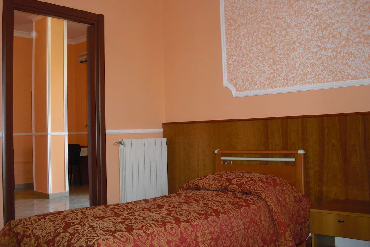 Un dormitorio con cabecera de madera, colcha estampada y radiador.