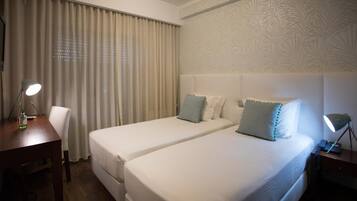 A hotel room with two single beds, a desk with a lamp, a chair, and a nightstand with a lamp.