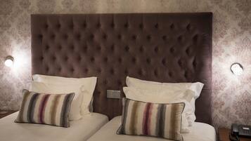 Quarto de hotel com cabeceira estofada, duas camas com roupa de cama branca, almofadas listradas e telefone ao lado da cama.