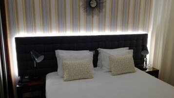 A hotel room with a large bed, two bedside tables, a wall clock, and a striped curtain.