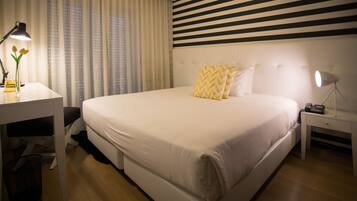 A hotel room with a large bed, a desk, a lamp, and a window with curtains.