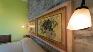 Una habitación con una cama, una pared de piedra y un cuadro floral enmarco.