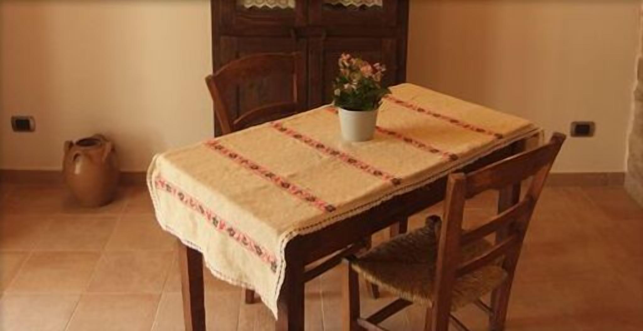 A dining table with a tablecloth, chairs, a potted plant, and a ceramic pot on the floor.